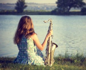 Demoiselle avec saxophone pensive au bort d'un fleuve. Coaching mental